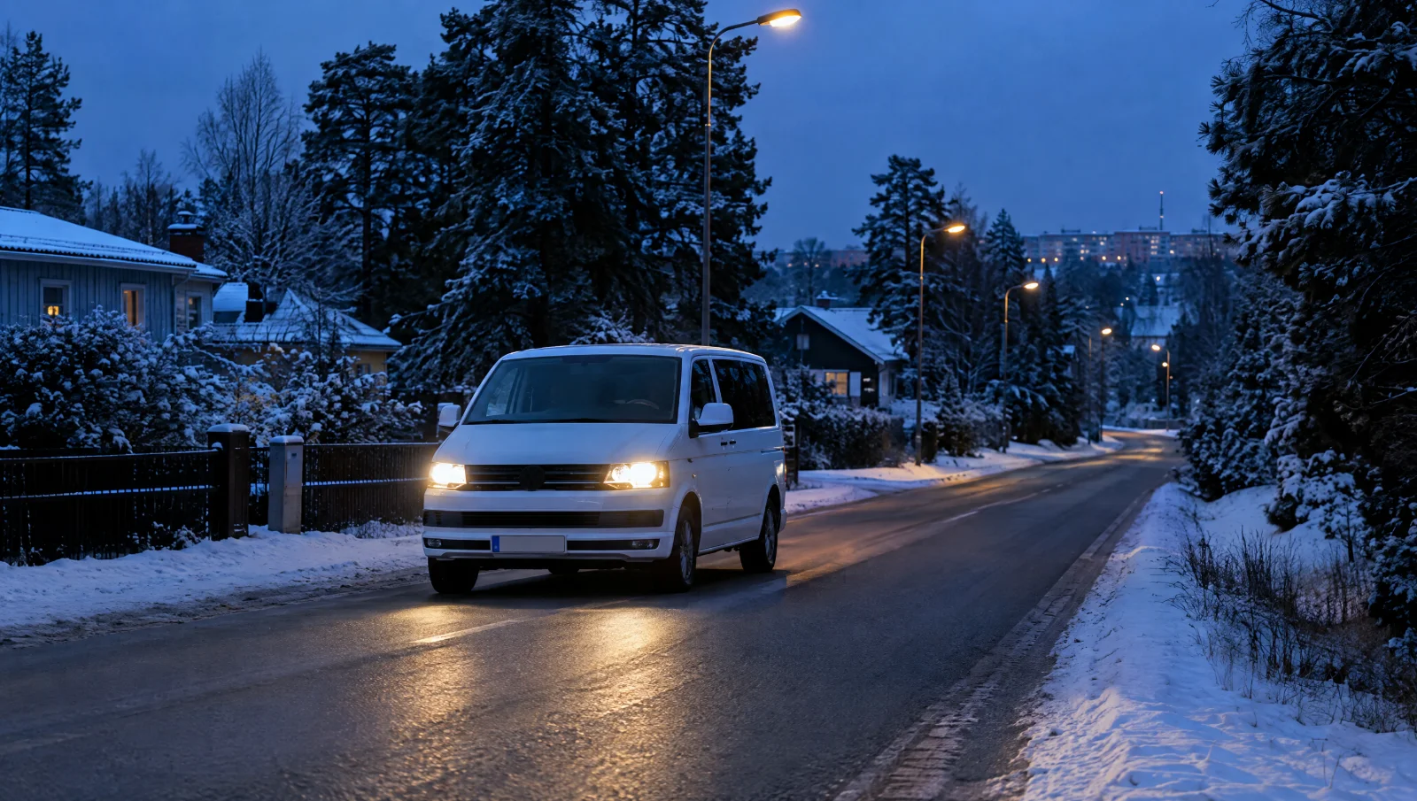 Vit minibuss med tända strålkastare på en snöig villagata en tidig vintermorgon